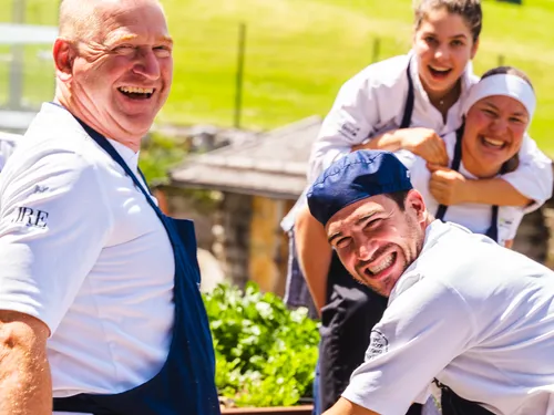 Lächelnde Köche in Uniform ernten gemeinsam Kräuter in einem sonnigen Garten
